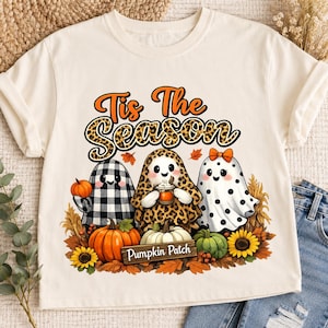 May include: A cream-colored t-shirt featuring a graphic of three ghosts in a pumpkin patch. The text reads Tis The Season and Pumpkin Patch. The ghosts wear buffalo plaid, leopard print, and polka dot patterns, surrounded by autumn foliage.