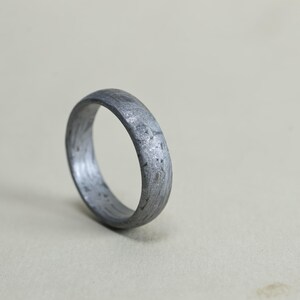 May include: A dark grey ring with a textured, mottled surface pattern resembling meteorite metal. The band has a rounded profile and a matte finish, displaying intricate, irregular geometric crystalline structures across the entire outer surface.