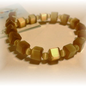 May include: A beaded bracelet featuring alternating cube and round beads in shades of brown and beige. The cube beads have a faceted appearance, and the bracelet is strung on an elastic cord. The bracelet is a jewelry accessory.