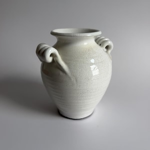 May include: A white ceramic vase with a bulbous body, a flared rim, and two decorative scrolled handles on the sides. The surface features a distinct crackle glaze finish, creating a network of fine lines across the entire exterior of the vessel.