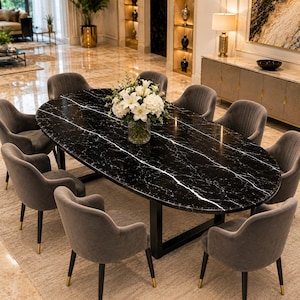 May include: An oval dining table with a black marble top featuring white veining, supported by a black metal base. The table is surrounded by eight grey upholstered armchairs with black legs and gold-toned tips, holding a glass vase of flowers.