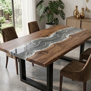 May include: A rectangular dining table featuring a natural live-edge wood slab with a central river-like inlay of grey and white swirling resin. The table is supported by two black metal U-shaped legs and is surrounded by four brown upholstered chairs.