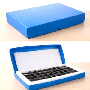 May include: A rectangular blue storage box with a hinged lid. The interior features a white foam lining and a black grid-style insert with multiple compartments for organizing small items. The box is shown both closed and open to reveal the interior.