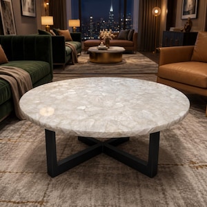 May include: A round coffee table featuring a polished white quartz stone top with a mosaic-like texture, supported by a sturdy black metal base with an intersecting cross-shaped design that provides a stable foundation for the circular tabletop.
