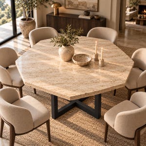 Puede incluir: Una mesa de comedor octogonal con una superficie de piedra beige moteada y una base de metal negro en forma de X. La mesa está rodeada por seis sillas beige tapizadas con patas de madera oscura. Un jarrón de piedra y dos candelabros están encima.