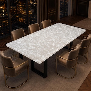 May include: A rectangular dining table with a white and light gray stone-look top featuring a mosaic pattern, supported by a black metal frame. Six upholstered brown chairs with gold-toned metal armrests and curved bases surround the table.