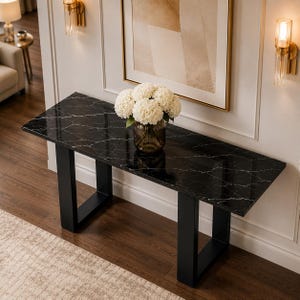 May include: A rectangular console table featuring a polished black marble top with white veining and two sturdy black metal U-shaped legs. A glass vase filled with a large bouquet of white hydrangea flowers sits centered on the table surface.