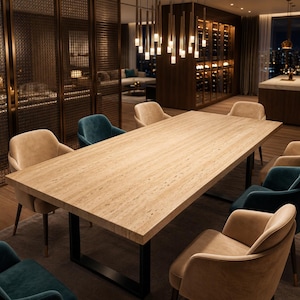 Puede incluir: Una mesa de comedor rectangular con tablero de piedra travertino en color beige claro y base de metal negro en forma de U. La mesa está rodeada por ocho sillones tapizados en terciopelo, alternando tonos beige suave y azul verdoso.