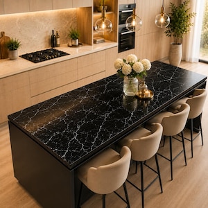 May include: A kitchen island featuring a black countertop with white veining, paired with four beige upholstered bar stools with black metal legs. A glass vase filled with white hydrangea flowers sits on the surface next to a small candle.