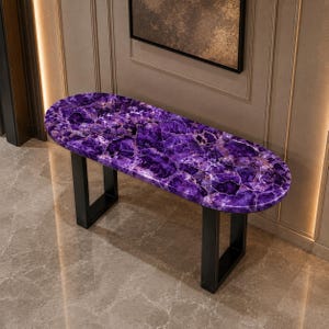 May include: An oval console table featuring a polished purple amethyst gemstone slab top with natural crystalline textures and deep violet hues, supported by two sturdy, matte black metal U-shaped legs that provide a stable base for the surface.