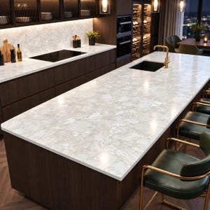 Puede incluir: Una isla de cocina con encimera de mármol blanco con vetas grises, grifo dorado y fregadero negro. La base es de madera oscura, acompañada de sillas de cuero verde con estructuras de metal dorado y respaldos curvos.
