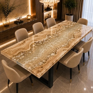 May include: A rectangular dining table featuring a polished stone surface with a central translucent resin inlay that mimics a flowing river, surrounded by six beige upholstered chairs with black legs and gold-toned metal accents at the feet.