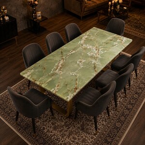 Può includere: Un tavolo da pranzo rettangolare con un piano in pietra onice verde chiaro lucido con venature bianche e dorate, sostenuto da una base in metallo dorato. Il tavolo è circondato da otto sedie imbottite grigio scuro con cuciture verticali.
