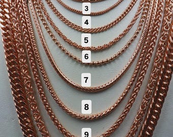 Könnte beinhalten: Eine Sammlung von elf roségoldfarbenen Metallketten auf einer Halsbüste, nummeriert von 1 bis 11. Die Ketten variieren in Dicke und Gliederart, von dünnen, feinen Anker- und Kugelketten bis hin zu dickeren, schweren Panzer- und geflochtenen Ketten.