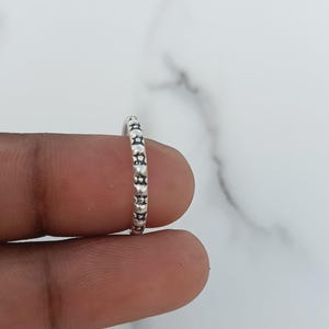 May include: A thin silver ring featuring a repeating pattern of small, raised circular dots and star-like shapes along the entire outer band. The metal has a slightly oxidised finish that highlights the intricate, textured detailing on the surface.