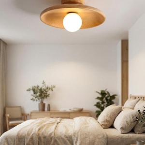 May include: A flush mount ceiling light fixture featuring a circular, light-toned wooden base and a wide, shallow, bowl-shaped wooden shade. A single, spherical, white frosted glass globe bulb is centred within the wooden shade, emitting light.