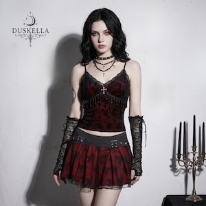 Puede incluir: Una camisola de terciopelo rojo oscuro con ribete de encaje negro, un pequeño colgante de cruz y una minifalda plisada a juego en rojo y negro con hebillas. El conjunto incluye calentadores de encaje negro y collar. Logo dice DUSKELLA.