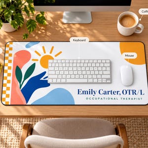 Op de afbeelding: Een rechthoekige bureaumat met een witte achtergrond en een kleurrijk abstract ontwerp van een gele zon, groene bladeren en blauwe vormen. De tekst Emily Carter, OTR/L OCCUPATIONAL THERAPIST staat in blauw en groenblauw in de rechterbenedenhoek.