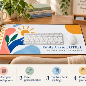 Op de afbeelding: Een rechthoekige bureaumat met een witte achtergrond, een gele zon, blauwe en roze abstracte vormen, groene bladeren en een oranje-witte geblokte rand. De tekst luidt Emily Carter, OTR/L OCCUPATIONAL THERAPIST in het blauw.