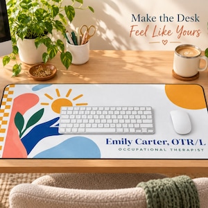 Op de afbeelding: Een rechthoekige bureaumat met een witte achtergrond, een gele zon, abstracte blauwe en koraalkleurige vormen en een geblokte rand. De tekst luidt Emily Carter, OTR/L OCCUPATIONAL THERAPIST. Een wit toetsenbord en een muis liggen op de mat.