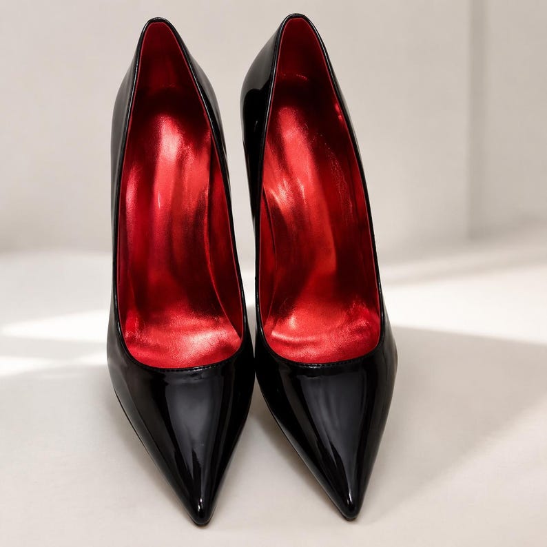 May include: A pair of black patent leather high heel pumps with a pointed toe design. The exterior of the shoes features a glossy black finish, while the interior lining and the footbed are a vibrant, metallic red color, creating a sharp contrast.