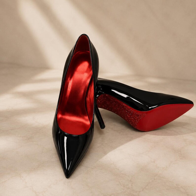 May include: A pair of black patent leather stiletto pumps with a pointed toe. The interior of the shoe is lined in a vibrant red satin material. The sole of the shoe is bright red, and the heel features a textured, sparkling red glitter finish.