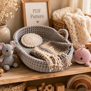 May include: A grey oval crochet basket containing a small cream-coloured circular mat and a striped brown and cream crochet blanket with fringe. A grey crochet mouse toy and a pink crochet whale toy are positioned beside the basket.