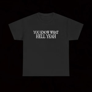 Può includere: Una t-shirt nera a maniche corte con il testo bianco YOU KNOW WHAT HELL YEAH stampato in un carattere serif al centro del petto. Il capo presenta uno scollo rotondo e una vestibilità standard, con un design grafico semplice e diretto.