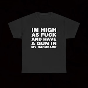 Może przedstawiać: Czarny t-shirt z krótkim rękawem z białym napisem na klatce piersiowej o treści: IM HIGH AS FUCK AND HAVE A GUN IN MY BACKPACK. Odzież posiada okrągły dekolt i standardowy krój, zaprezentowana na jednolitym czarnym tle.