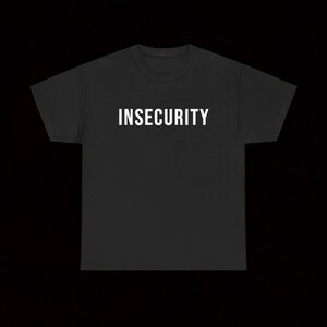 Könnte beinhalten: Ein schwarzes Kurzarm-T-Shirt mit dem Wort INSECURITY, das in fetten weißen Großbuchstaben mittig auf der Brust aufgedruckt ist. Das Kleidungsstück hat einen klassischen Rundhalsausschnitt und einen geraden Saum auf schwarzem Grund.