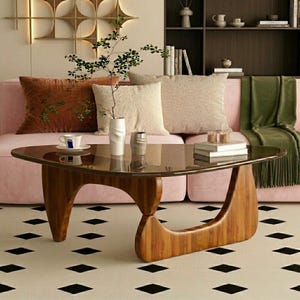 May include: A coffee table with a triangular glass top and a curved wooden base. The table features a smooth, dark-toned wood frame with an open, sculptural design. A white ceramic vase with a leafy branch sits on the glass surface.