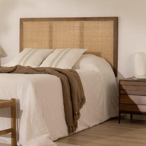 May include: A rectangular headboard featuring a natural woven rattan panel framed in dark brown wood. The headboard is positioned behind a bed dressed in white linens, two white pillows with beige stripes, and a textured brown throw blanket.