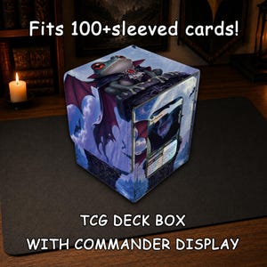 Puede incluir: Una caja cuadrada para barajas TCG con ventana de visualización, que muestra una rana vampiro con ojos rojos y alas moradas sobre una repisa de piedra. La caja incluye el texto Fits 100+sleeved cards! TCG DECK BOX WITH COMMANDER DISPLAY.