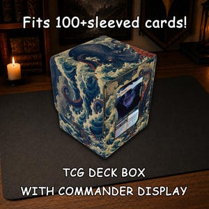Op de afbeelding: Een vierkante TCG-deckbox met een displayvenster, voorzien van een print van een blauwe octopus en oceaangolven. De tekst luidt: Fits 100+sleeved cards! TCG DECK BOX WITH COMMANDER DISPLAY. De box bevat één ruilkaart in het voorste venster.
