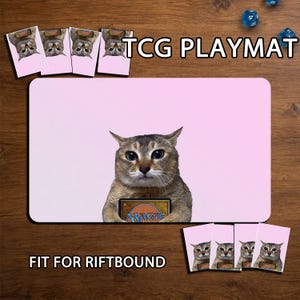 May include: A rectangular TCG playmat featuring a light pink background and a central image of a brown cat holding a Magic: The Gathering card. The text TCG PLAYMAT and FIT FOR RIFTBOUND is visible, along with smaller matching cat card sleeves.