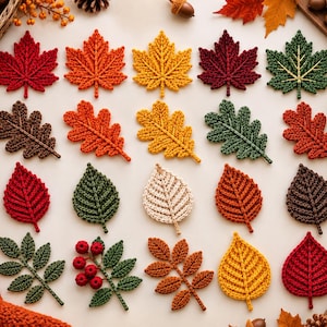 May include: A collection of twenty crocheted leaves and botanical elements in various autumn colors including red, orange, yellow, green, brown, and cream. The set features maple, oak, and birch leaf shapes, along with a sprig of red berries.