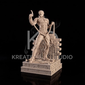 May include: A beige monochromatic figurine of a humanoid character with a textured, muscular suit, holding a long chain that drapes across the body. The figure stands on a rectangular base in front of a brick wall section with dripping details.