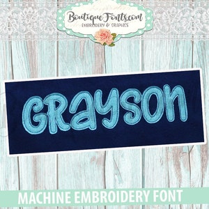 May include: Machine embroidery font design for the name Grayson. The font is blue and outlined in a darker blue. The design is on a dark blue background.