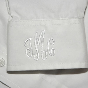 May include: White cotton shirt cuff with a white embroidered monogram of the letters "JMC".