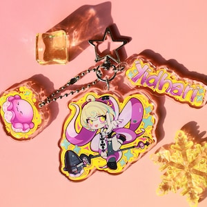 May include: A clear acrylic keychain featuring a central charm of an anime-style character with blonde hair and purple tentacles holding a staff, a smaller pink octopus charm, and a name tag reading Yidhari, all attached to a silver star clasp.