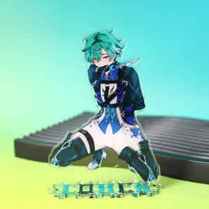 May include: An acrylic standee featuring an anime-style character with teal hair and red eyes, wearing a blue and white outfit with black straps and thigh-high boots. The character is in a kneeling pose on a base with blue text printed on it.