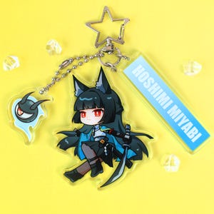 May include: An acrylic keychain featuring a chibi character with black hair, fox ears, and red eyes, wearing a blue and black outfit with a sword. It includes a small ghost-like charm, a rectangular tag reading HOSHIMI MIYABI, and a star-shaped clasp.