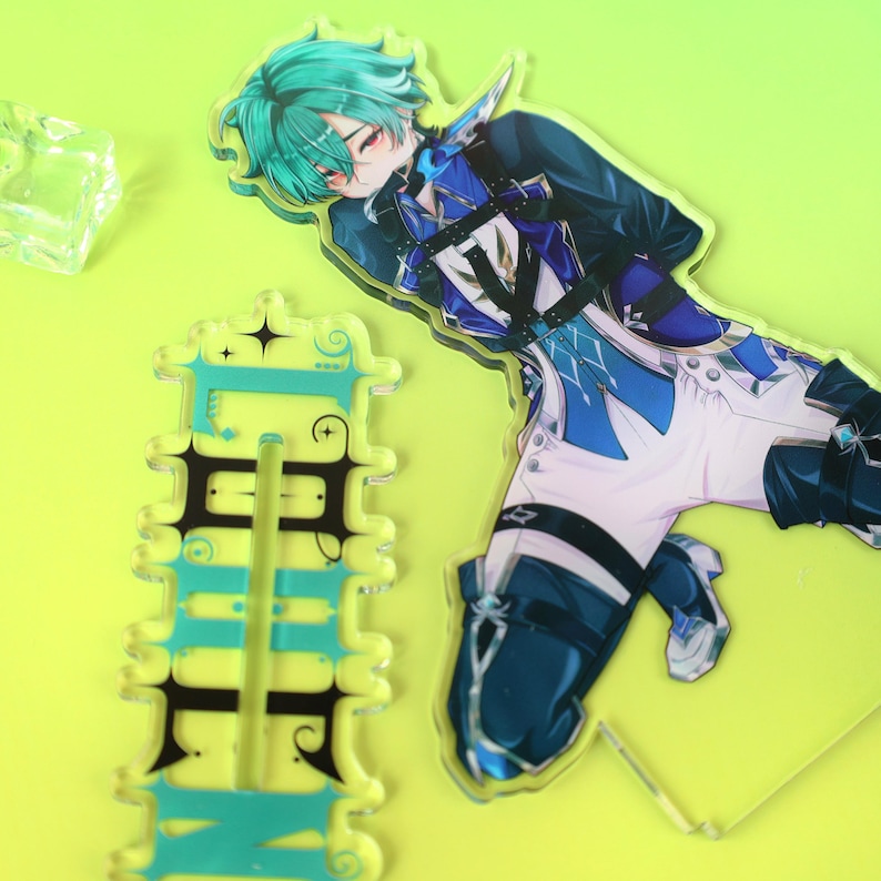 May include: An acrylic standee featuring an anime-style character with teal hair, wearing a blue and white outfit with black straps. Beside it is a rectangular acrylic base with decorative black scrollwork and teal accents printed on the surface.
