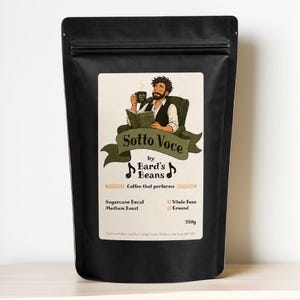 May include: A black coffee bag with a cream-coloured label featuring an illustration of a person reading a book while holding a mug. The text reads Sotto Voce by Bard's Beans, Coffee that performs, Sugarcane Decaf, Medium Roast, and 250g.
