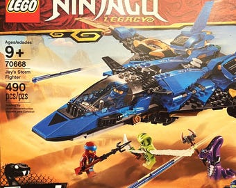 May include: A LEGO Ninjago Legacy Jay's Storm Fighter building set box, model 70668, featuring a blue jet with gold accents, a cockpit, and four minifigures. The box displays the 490-piece count, age rating 9+, and a desert scene with characters.