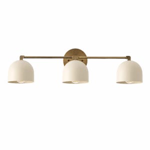 May include: A three-light wall fixture featuring a horizontal brass bar and a circular brass wall plate. Three matte cream-colored dome-shaped shades are evenly spaced along the bar, each housing a single light bulb pointing downward.