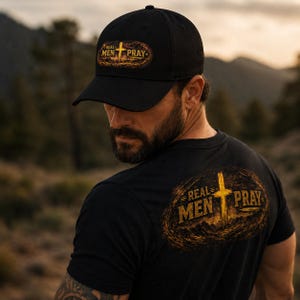 Peut inclure: Une casquette de baseball noire et un t-shirt noir, tous deux ornés d'un motif graphique représentant une croix dorée et le texte "REAL MEN PRAY" sur un fond texturé, sombre et usé. Le motif est centré sur la casquette et le dos du t-shirt.