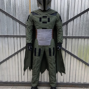 Puede incluir: Un disfraz de cuerpo completo que incluye un casco plateado met&aacute;lico con visera en forma de T, una chaqueta de manga larga verde oliva con pantalones a juego, una placa abdominal gris, guantes negros, zapatos negros y una capa verde oscuro.