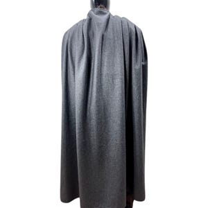 May include: A floor-length, charcoal gray cape featuring a high collar and a structured, draped silhouette. The garment is crafted from a solid-colored, textured fabric that falls in vertical folds from the shoulders down to the hemline.