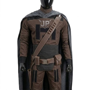 May include: A brown and black tactical costume set featuring a long grey cape, a brown long-sleeve shirt with black panels and the letters JP on the chest, a brown utility belt with a holster and pouch, and a diagonal shoulder strap with loops.